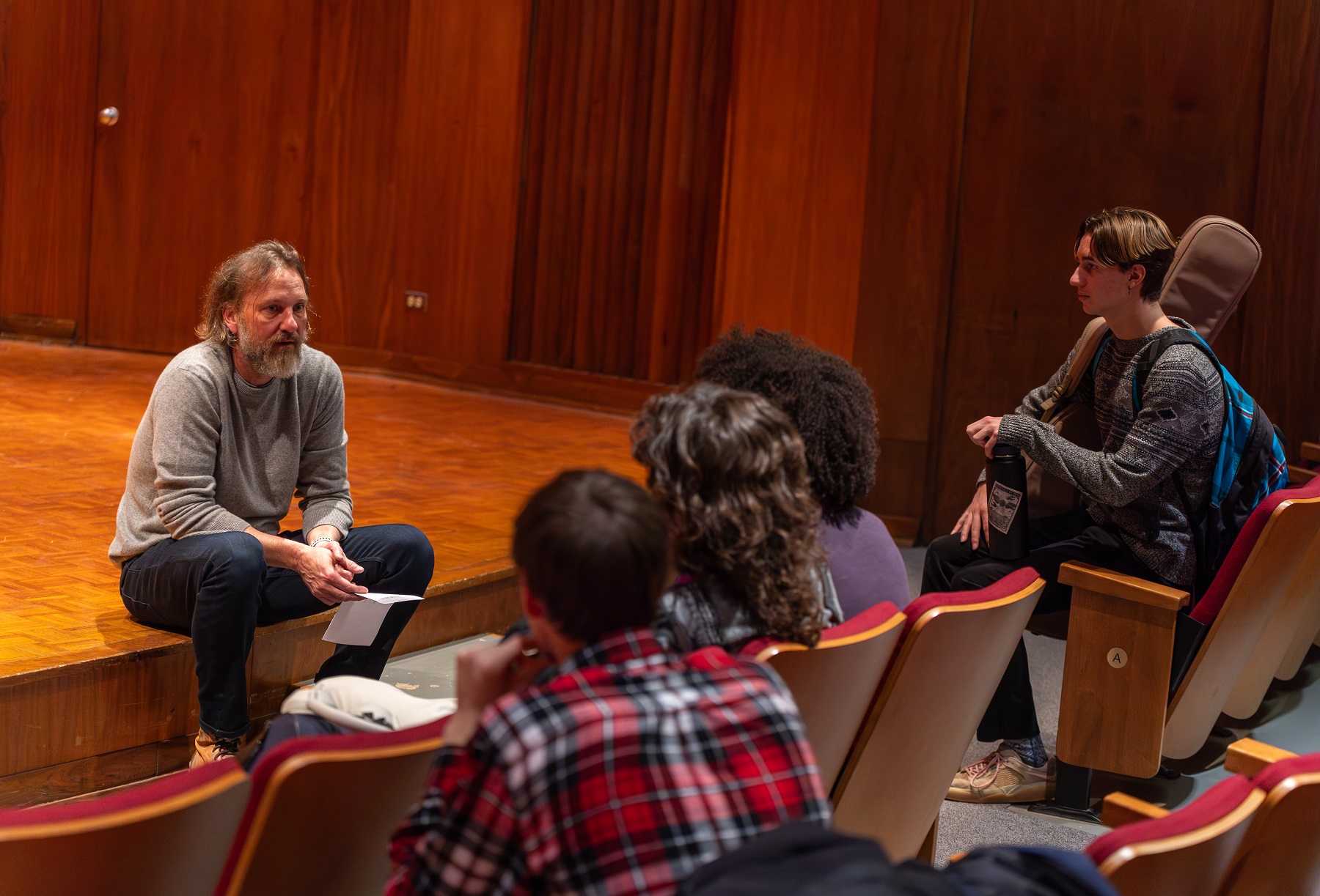 Michael Smith sits on the stage in Harper Hall as he talks to students in the songwriting class.