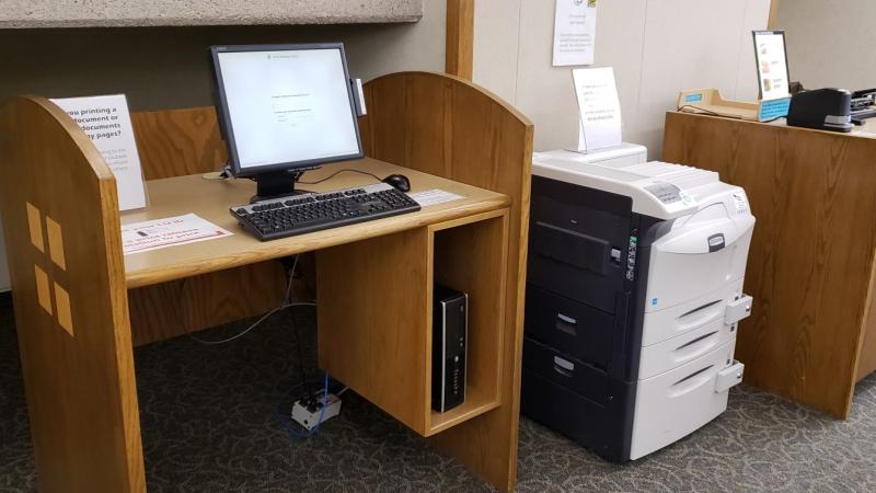 Computer at a table with print release software next to a large printer.