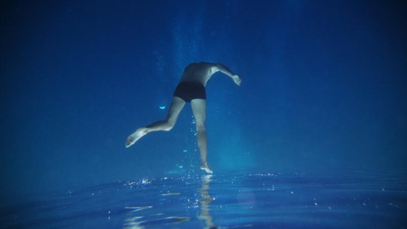Dancer performing underwater, surface of water at the bottom of the frame so dancer seems to be upright while being upside down underwater