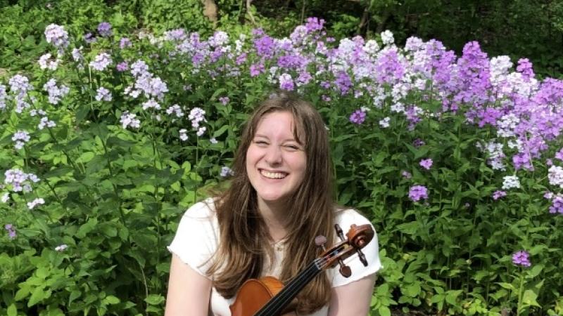 Mallory Welsch holds a violin in front of flowers.