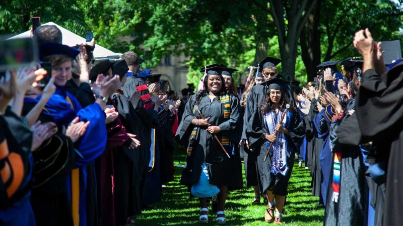 Graduates walk through the faculty line as faculty applaud during the processional at the start of Commencement.