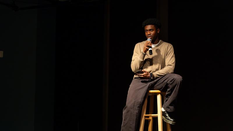 A student sits on a stool on stage during his performance.