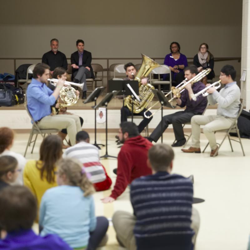 Students perform for people seated on a floor.