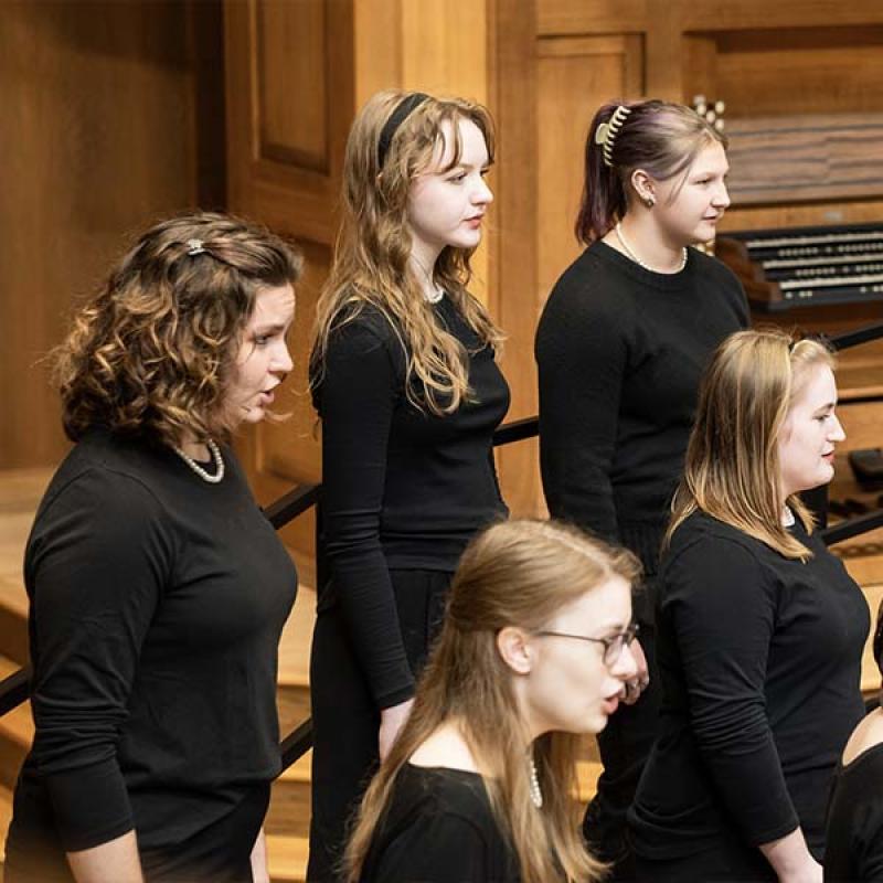 Five women dressed in concert black sing on the Chapel stage during a concert