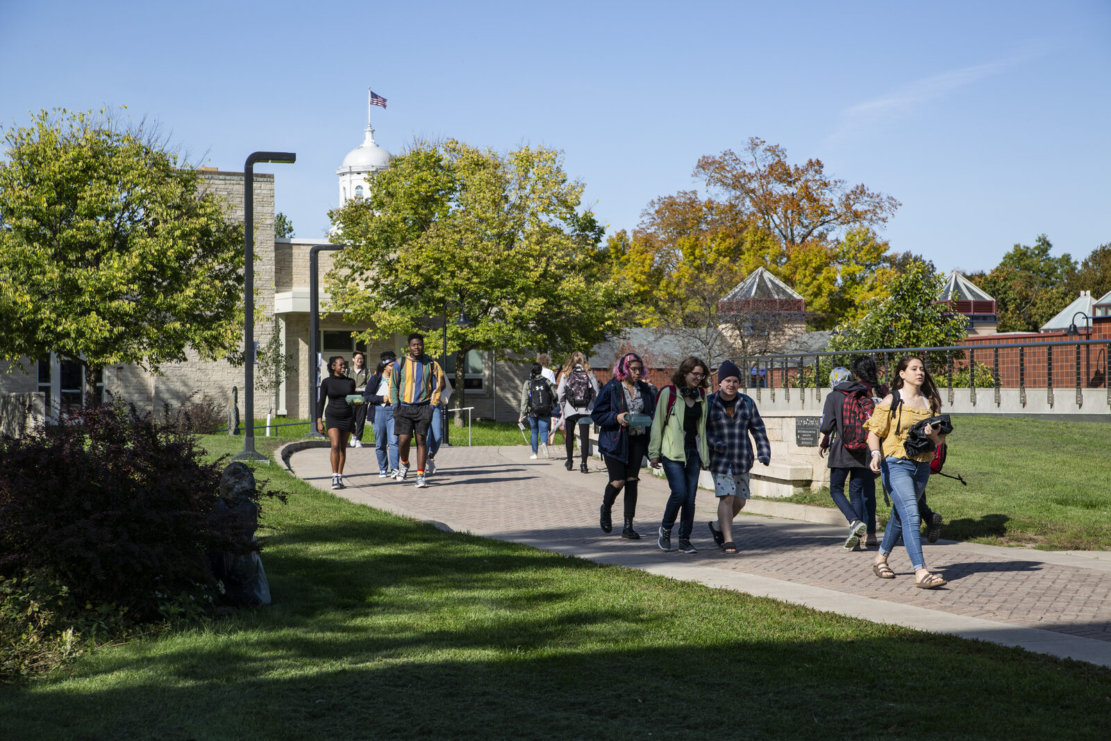 Lawrence students walking on a paved path with an academic hall in the background. Students are in small groups smiling and talking.