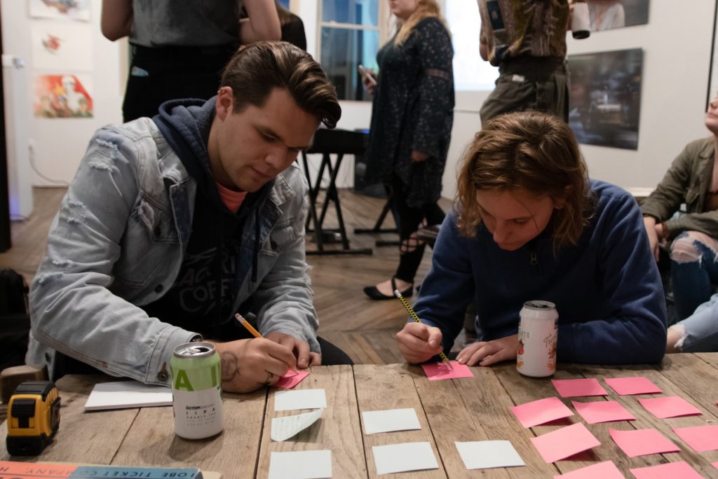 Two students writing on sticky notes at an art show.