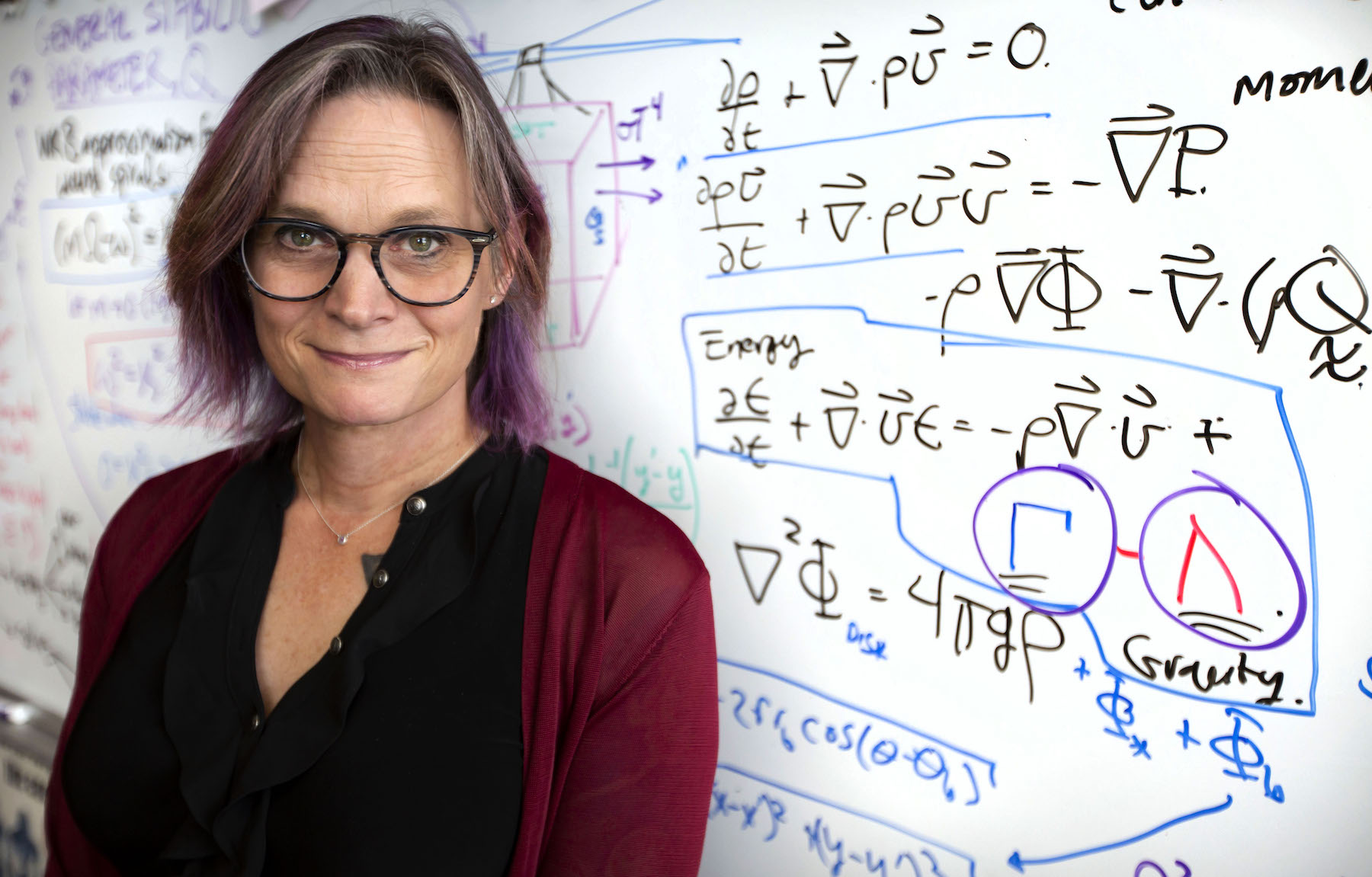 Megan Pickett stands in front of a whiteboard with physics equations.