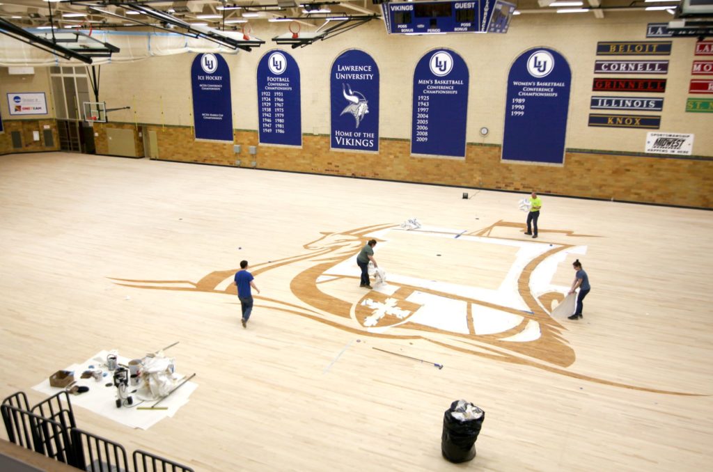 Workers prepare the logo on the refurbished floor in Alexander Gym.