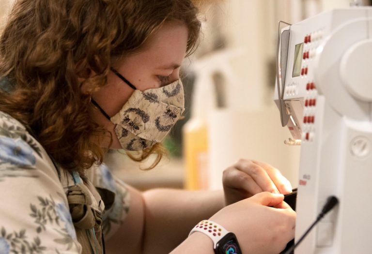 Work stations in the costume shop have been adjusted keep student workers safe. Here, Isabel Kelly ’21 works on a flute mask at one of the sewing machines.