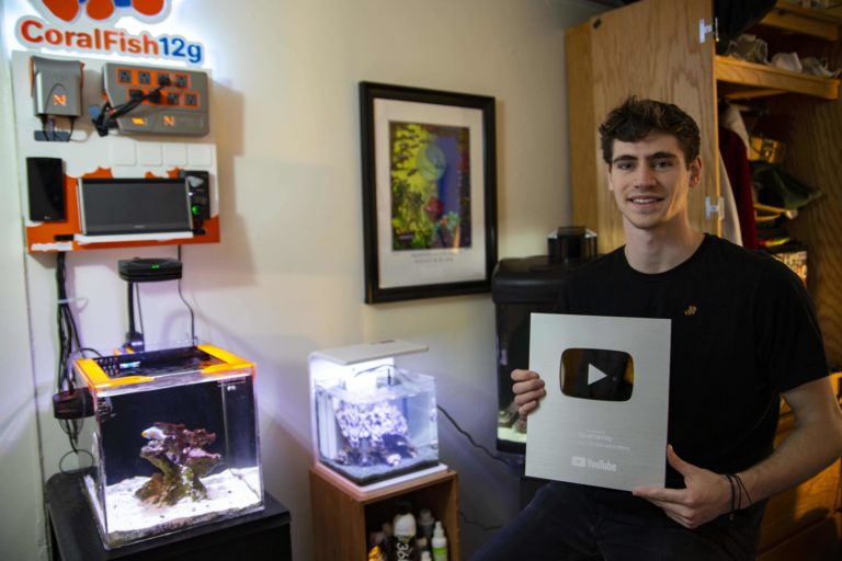 Geogre George Mavrakis holds up his silver play button from Youtube as he stands in front of his fish tank.