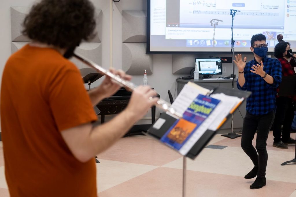 member of the Mariachi Ensemble playing the flute and other member clapping 