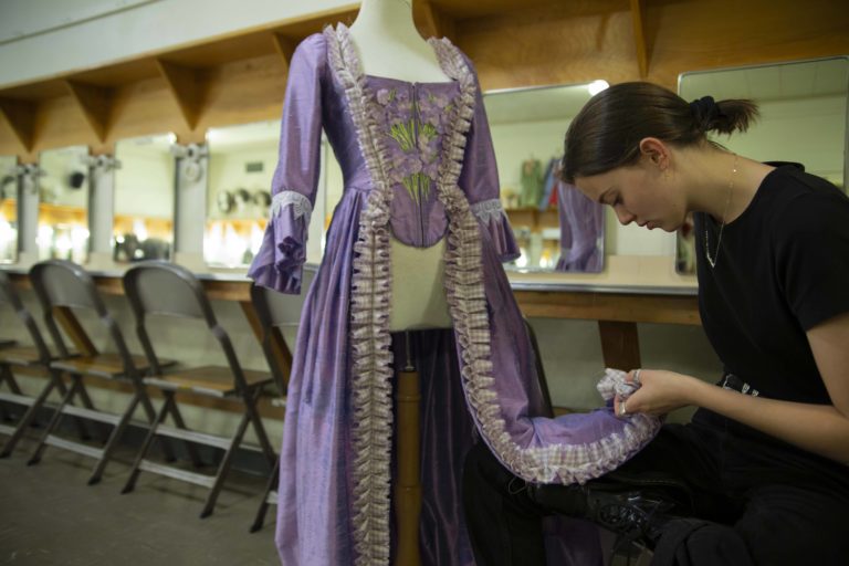 Mads Layton bends over to look at the hemline of a purple costume.