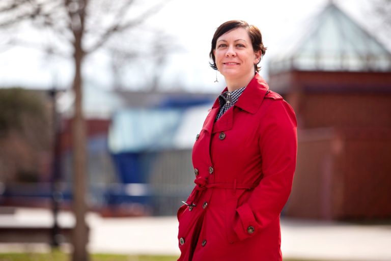 Beth Zinsli, wearing a long red jacket, stands in front of the Wriston Art Center.