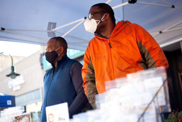 Yaw Asare stands next to his business partner in their booth at the Farmers Market.