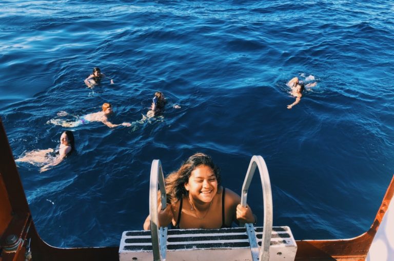 Naomi Torres-Solorio climbs down a ladder into the ocean where five other people are swimming.