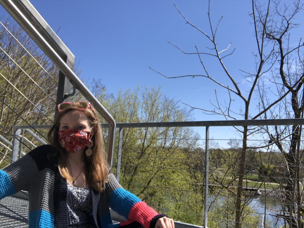 Student sitting in a flight of metallic stairs with the Fox River in the background 