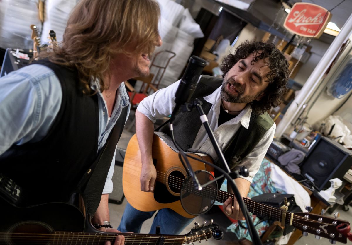 Rob Neilson and Jake Frederick playing the guitar and singing into a mic 