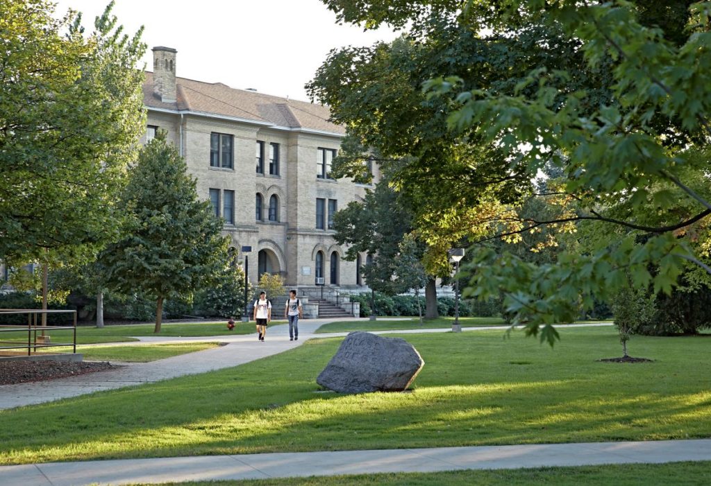 Two students walking across Main Hall Green surrounded by trees  