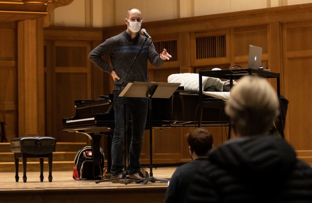 Professor Sieck taking to his class in the Memorial Chapel stage with a piano behind him 