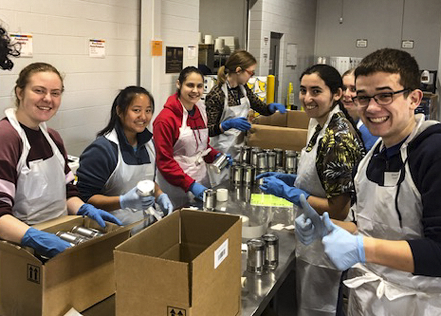 Students using gloves and aprons smiling at the camera while volunteering  