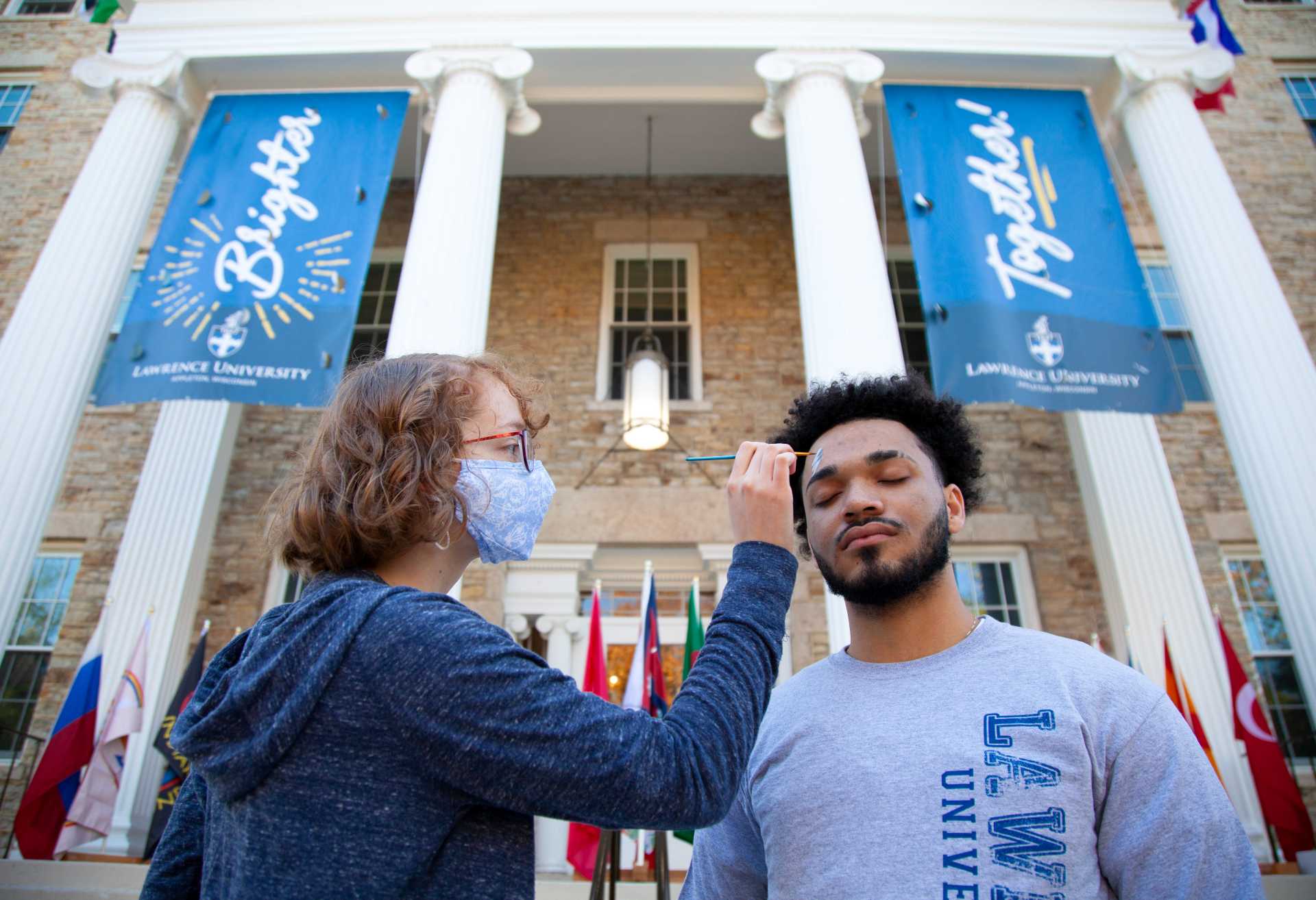 Claire Chamberlin, a junior, paints the face of Jose Otero. A first-year, during the Blue and White Weekend Block Party on Main Hall Green.