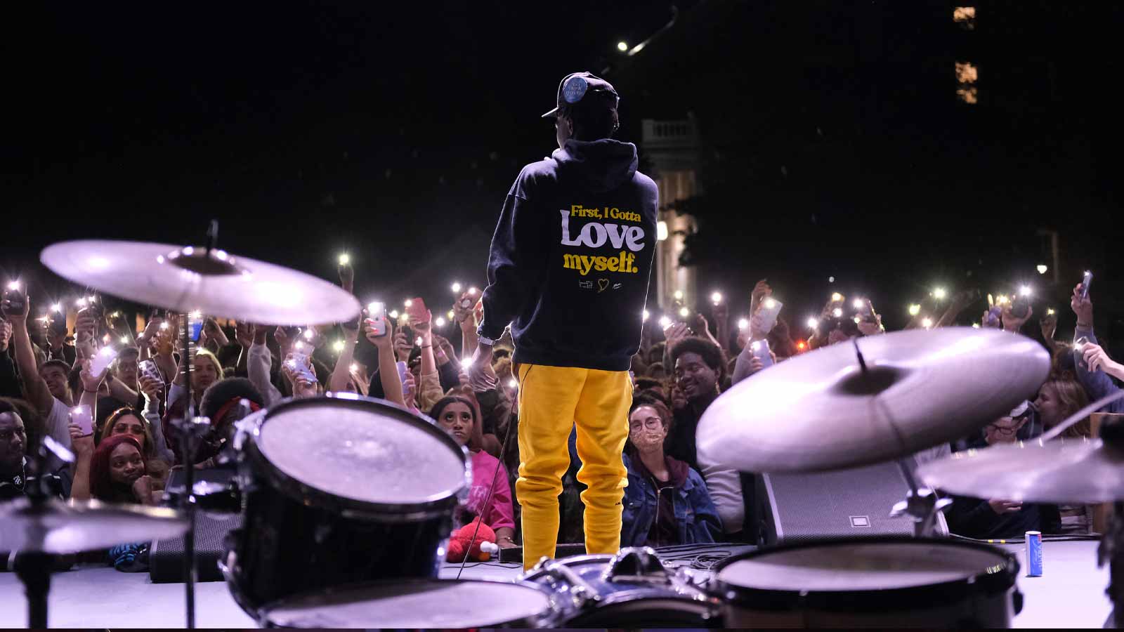 Image of a man on stage with and audience with their phone lights on