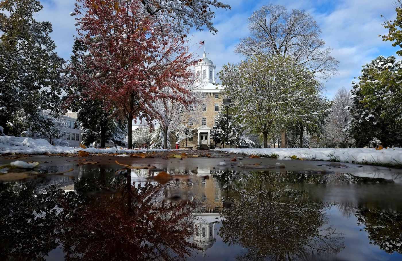 Main Hall reflection in puddle on sidewalk. There is snow on the ground.