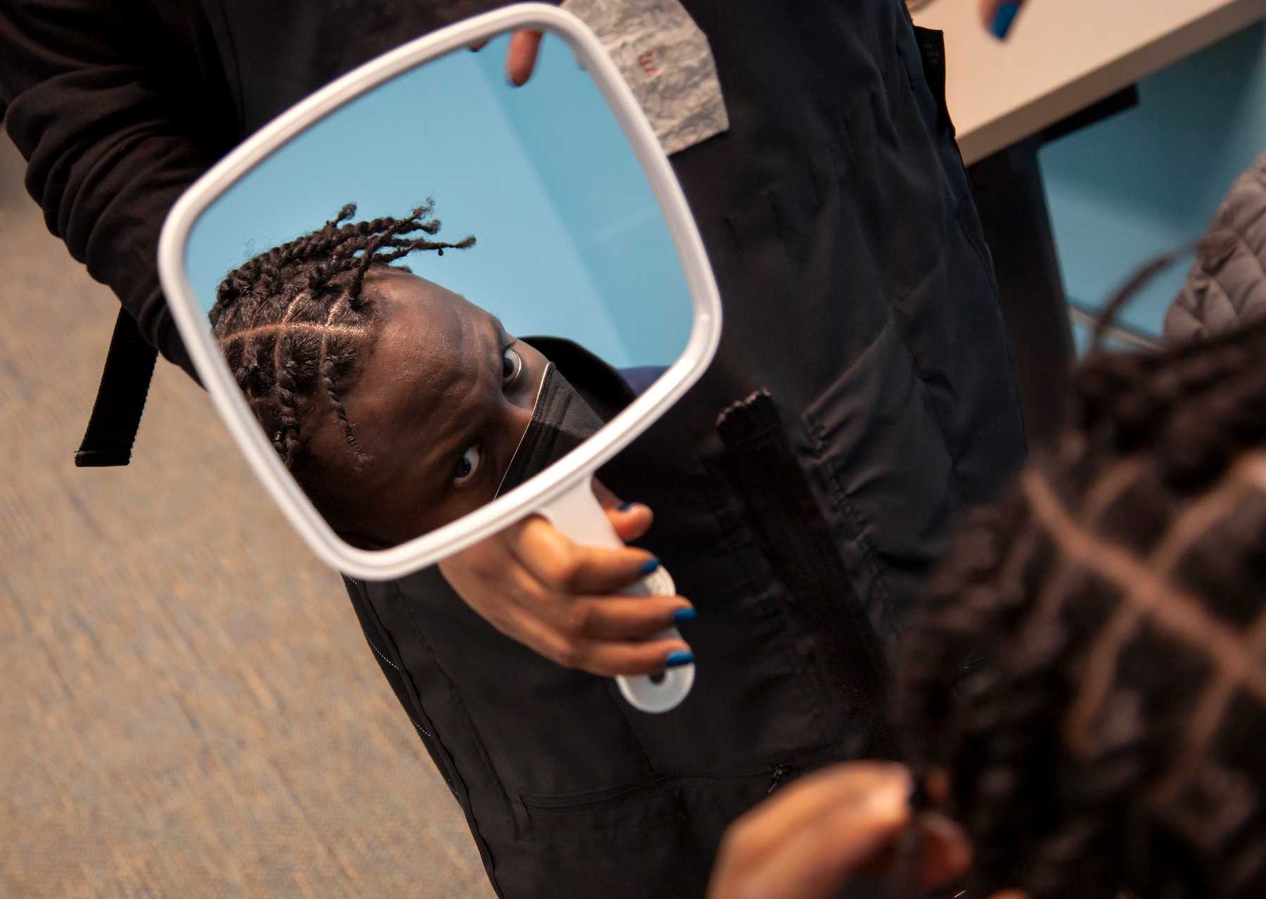 Eder Bellegarde looks up at a small mirror being held by Elle Tolan of Taperz Barber Shop. 