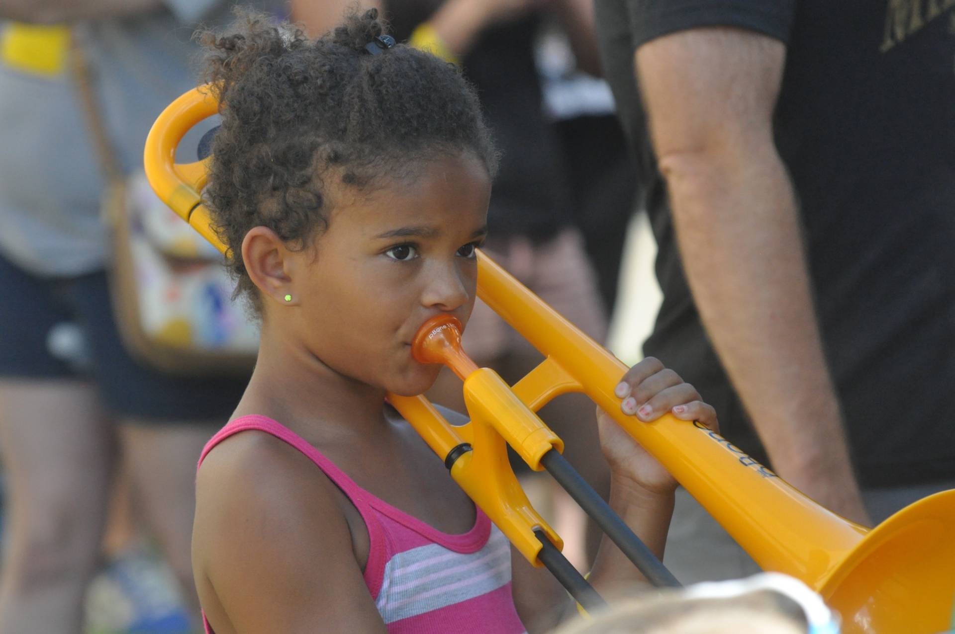 Toddler "playing" blowing into a giant yellow trumpet.