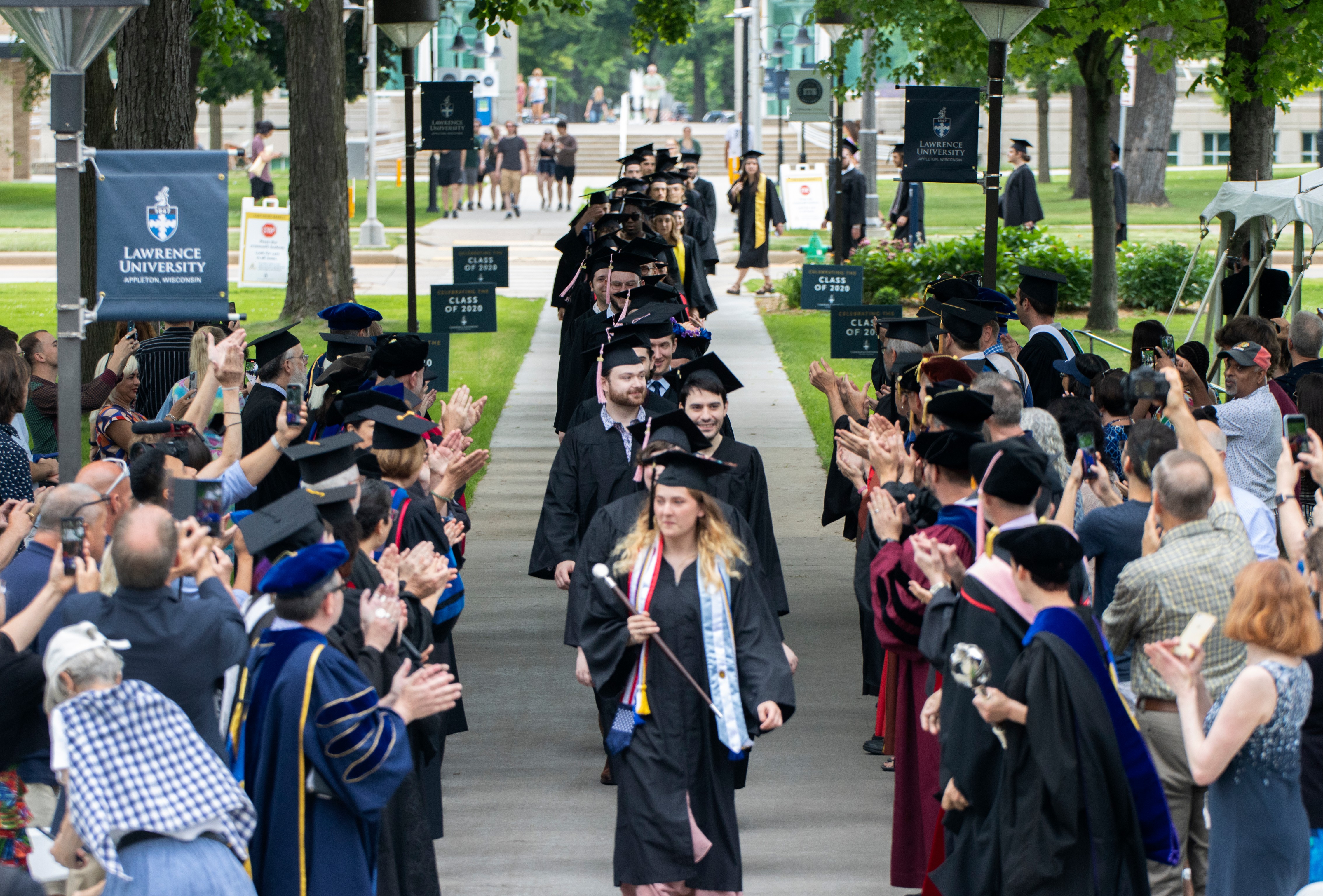 Graduates dressed in cap and gown process between rows of faculty dressed in regalia.