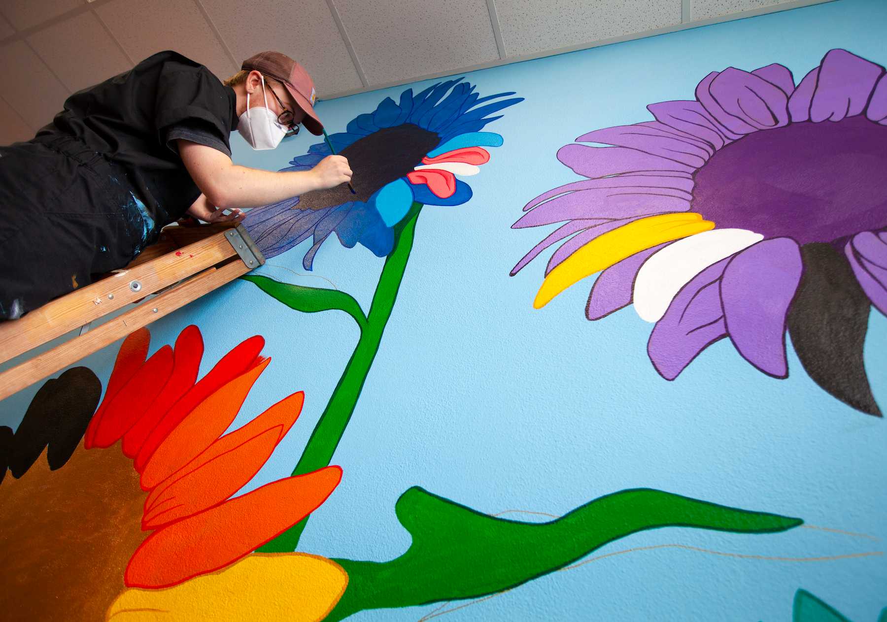 Cael Neary stands on a ladder as he paints the mural.