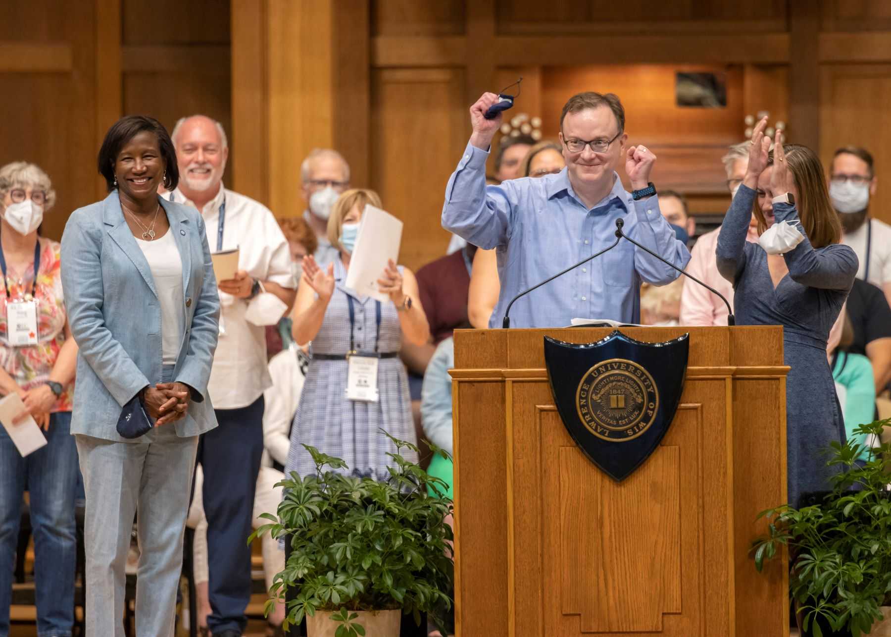 David Bauman pumps his fist at the podium as he presents the class gift while President Laurie Carter and other alumni look on on the stage of Memorial Chapel.