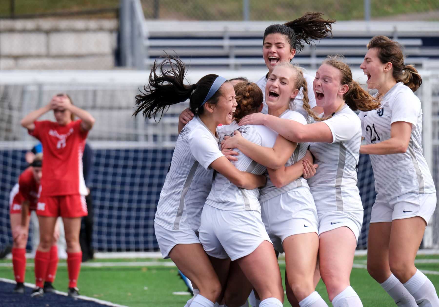 Members of the Lawrence women's soccer team celebrate in the moments after a game-winning goal is scored while members of the opposing team show dejection in the background.
