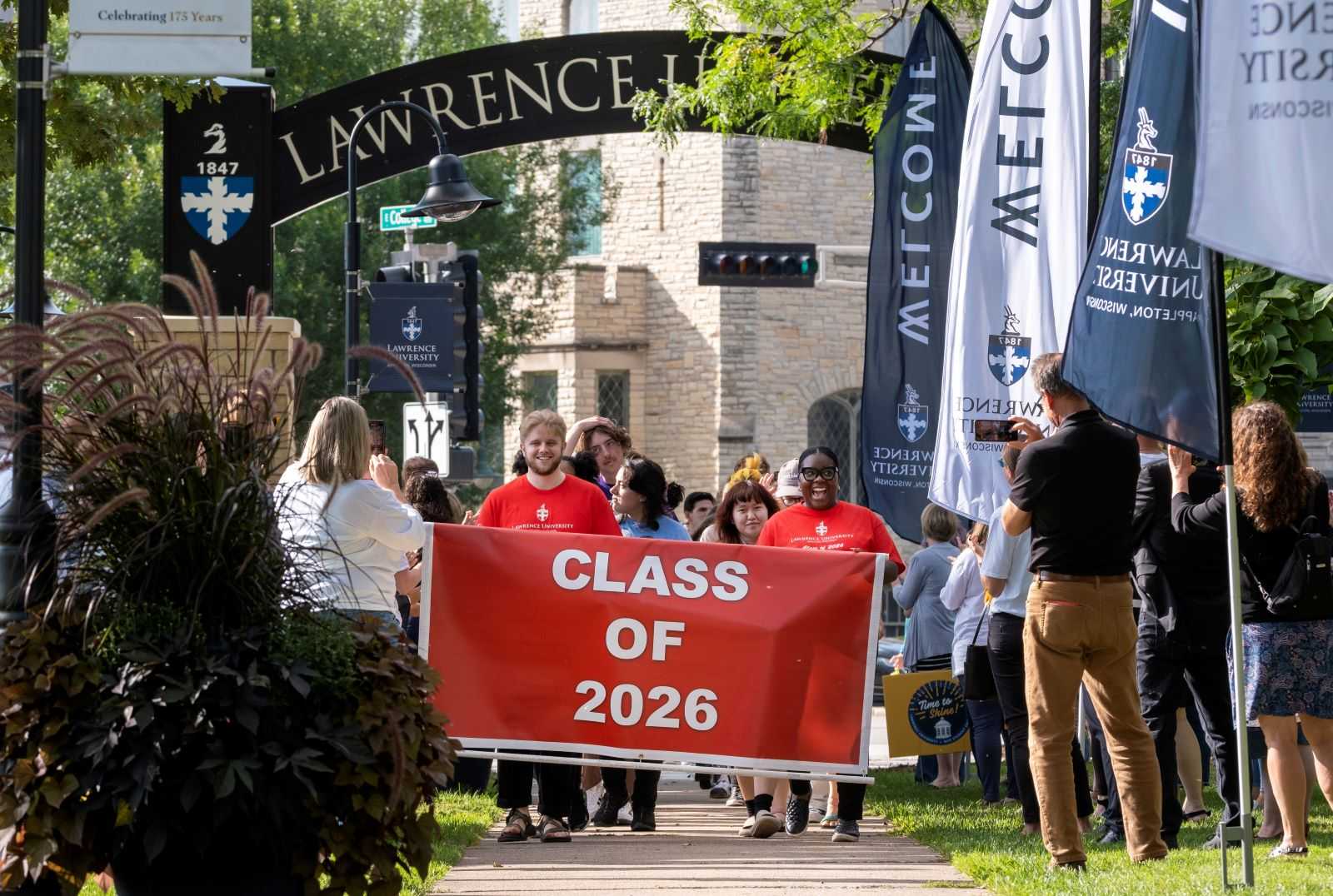 Incoming students carry the red Class of 2026 flag as they lead the processional under the arch.