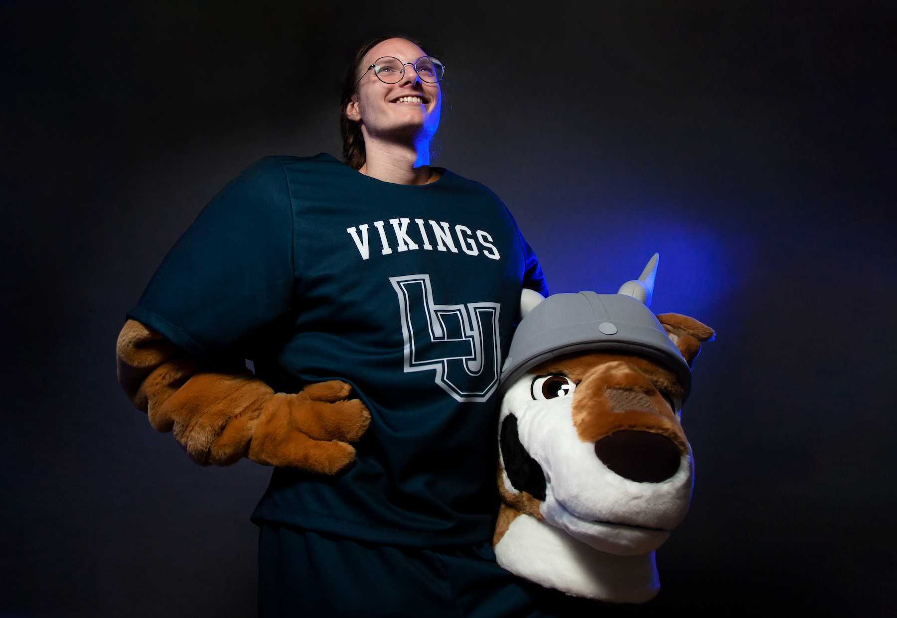 Spencer Brown poses for a photo bathed in blue light while holding the head of the Blu mascot.