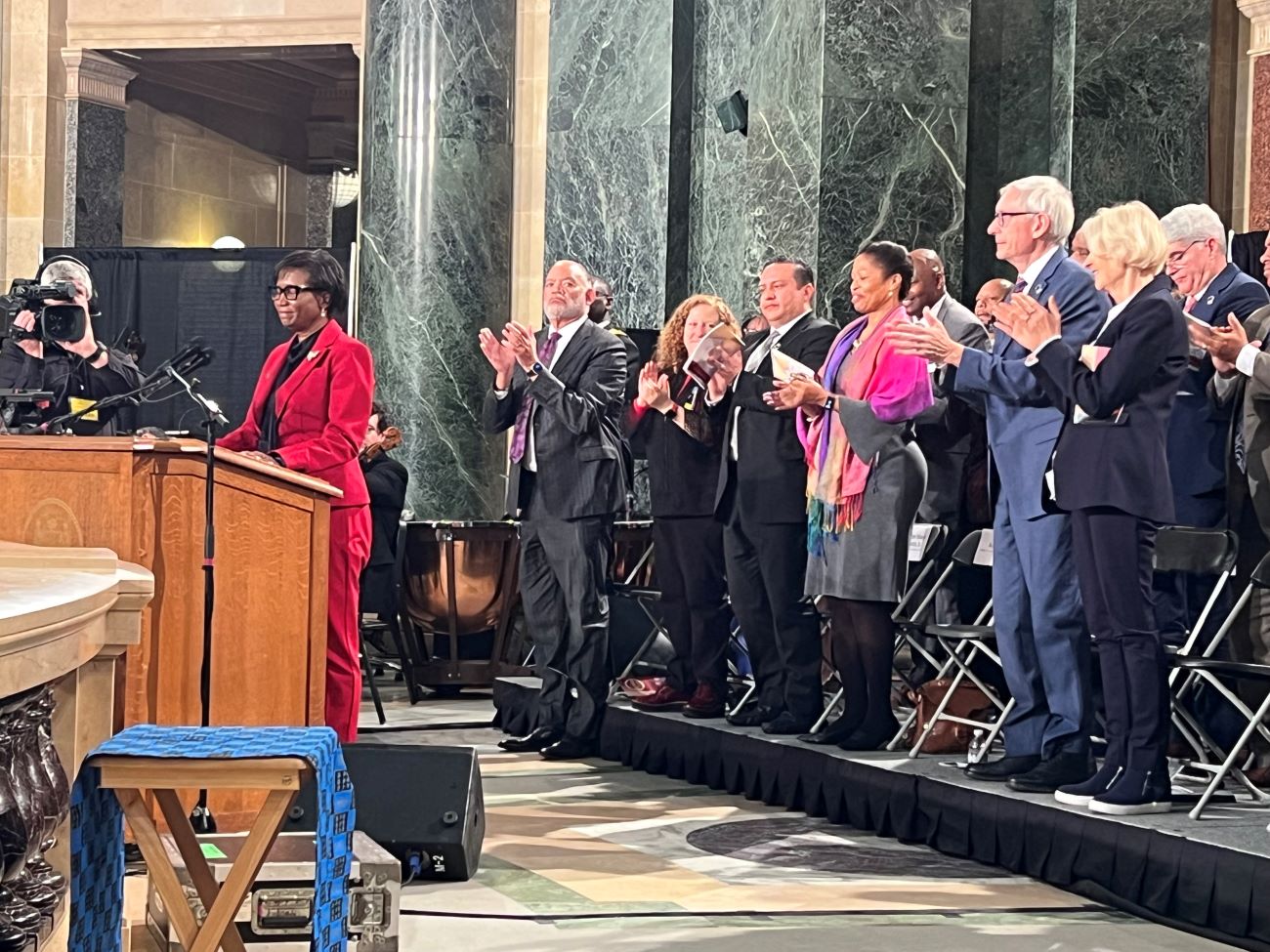 President Laurie Carter speaks at the podium as Gov. Evers and others applaud.
