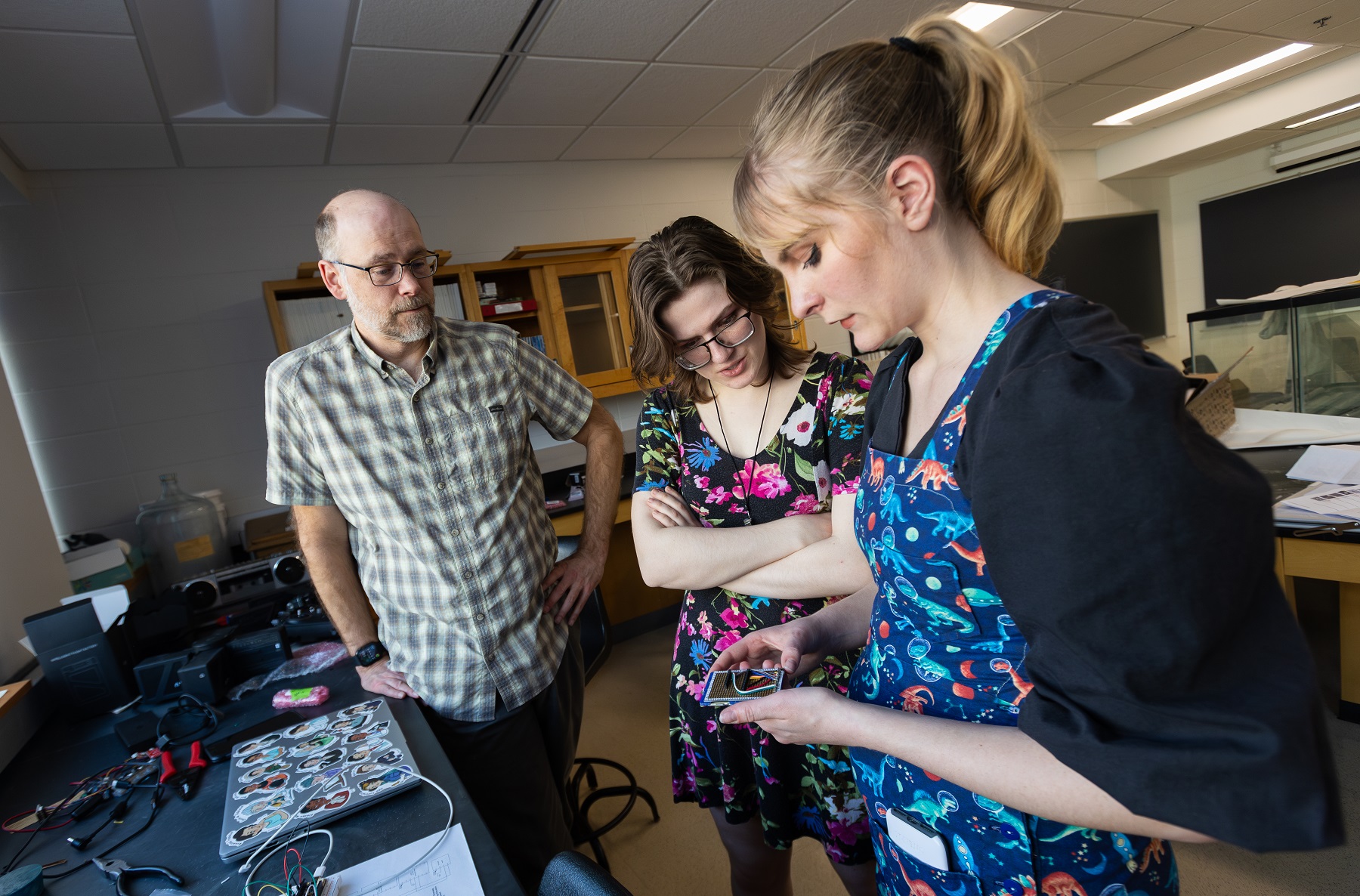 Jeff Clark and Kat McClain look on as Sydney Closson works through the wiring of a spectrometer. 