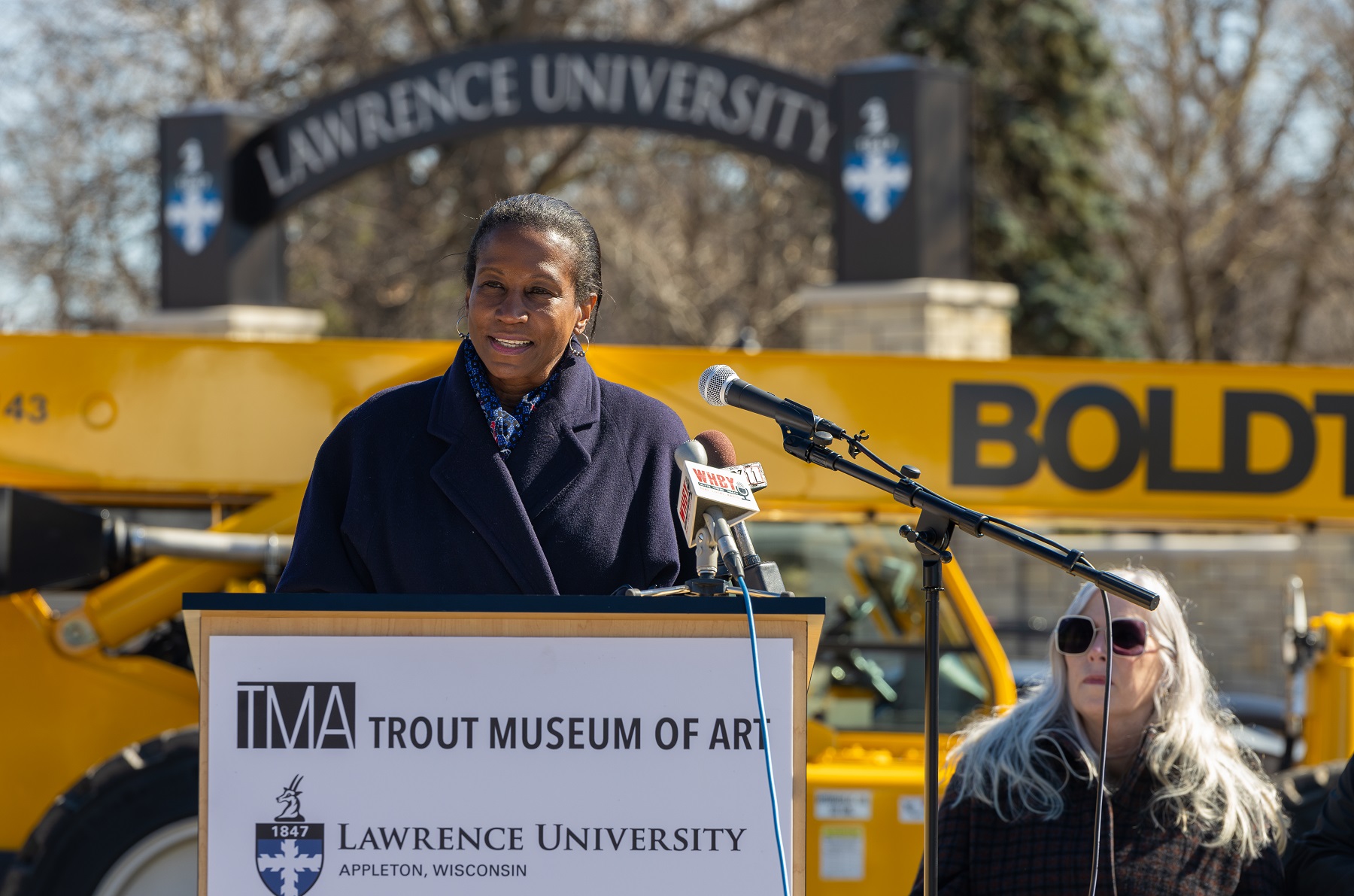 Lawrence University President Laurie A. Carter speaks at the podium during the groundbreaking ceremony. The Lawrence Arch is in the background across Drew Street.