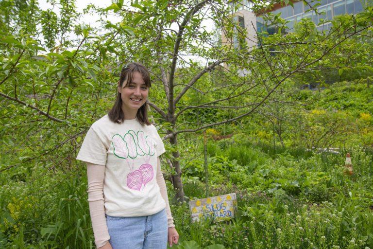 Phoebe Eisenbeis stands amid greenery with a small "SLUG Garden" sign on the ground.