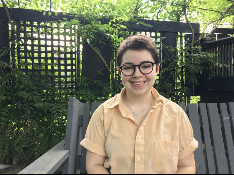 Emily Harper, wearing a yellow button-up shirt, smiles against a backdrop of greenery.