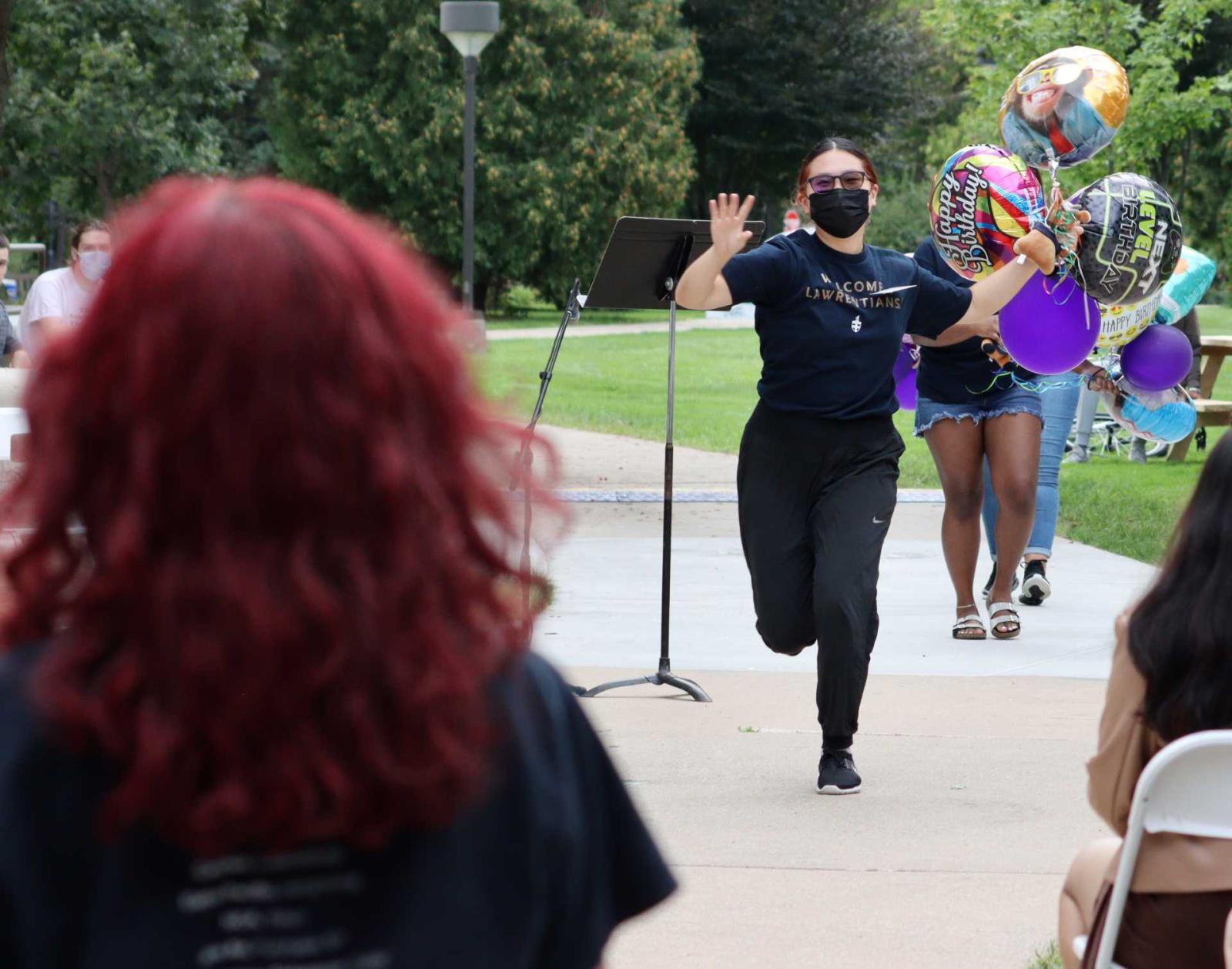 Student Orientation Leader running toward incoming student with birthday balloons.