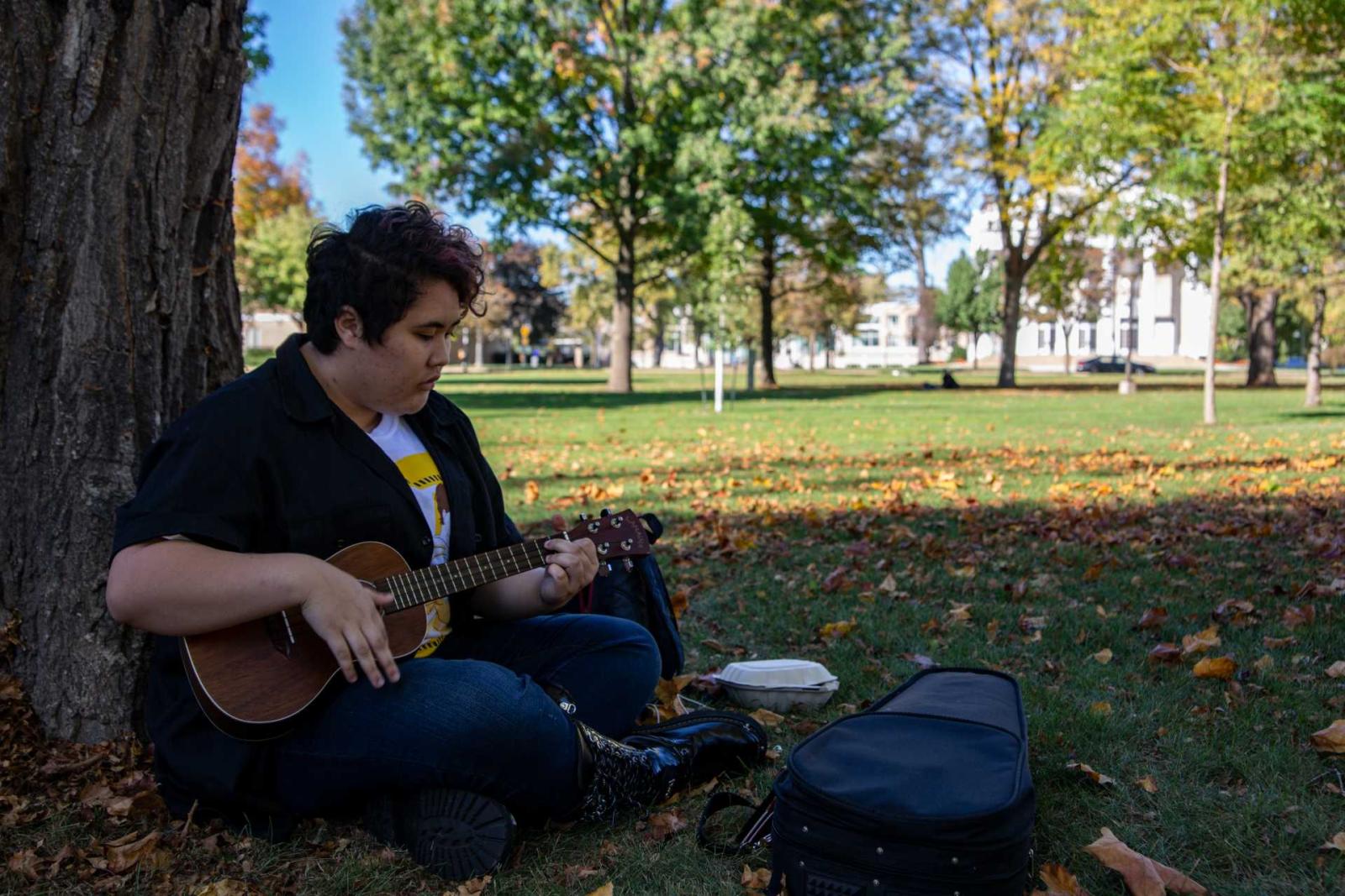 Lawrence student, Mahina Olores, sitting on Main Hall Green practicing the ukulele