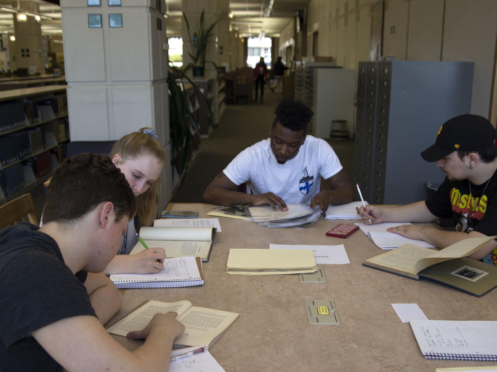 Group of students sitting at a table in the library looking at papers from the university archives.