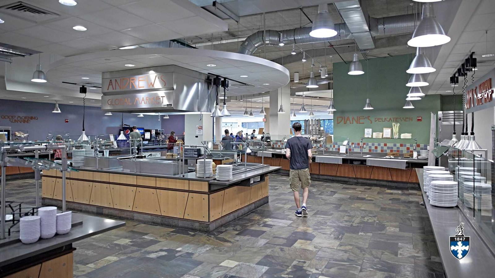 Student walking into buffet food stations in large, open cafeteria.