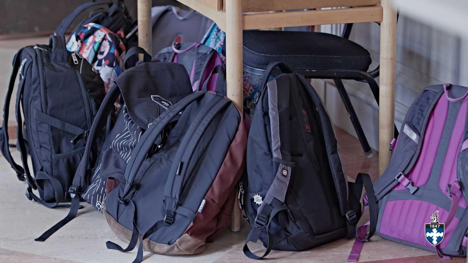 Seven backpacks lying near foot of dining table.