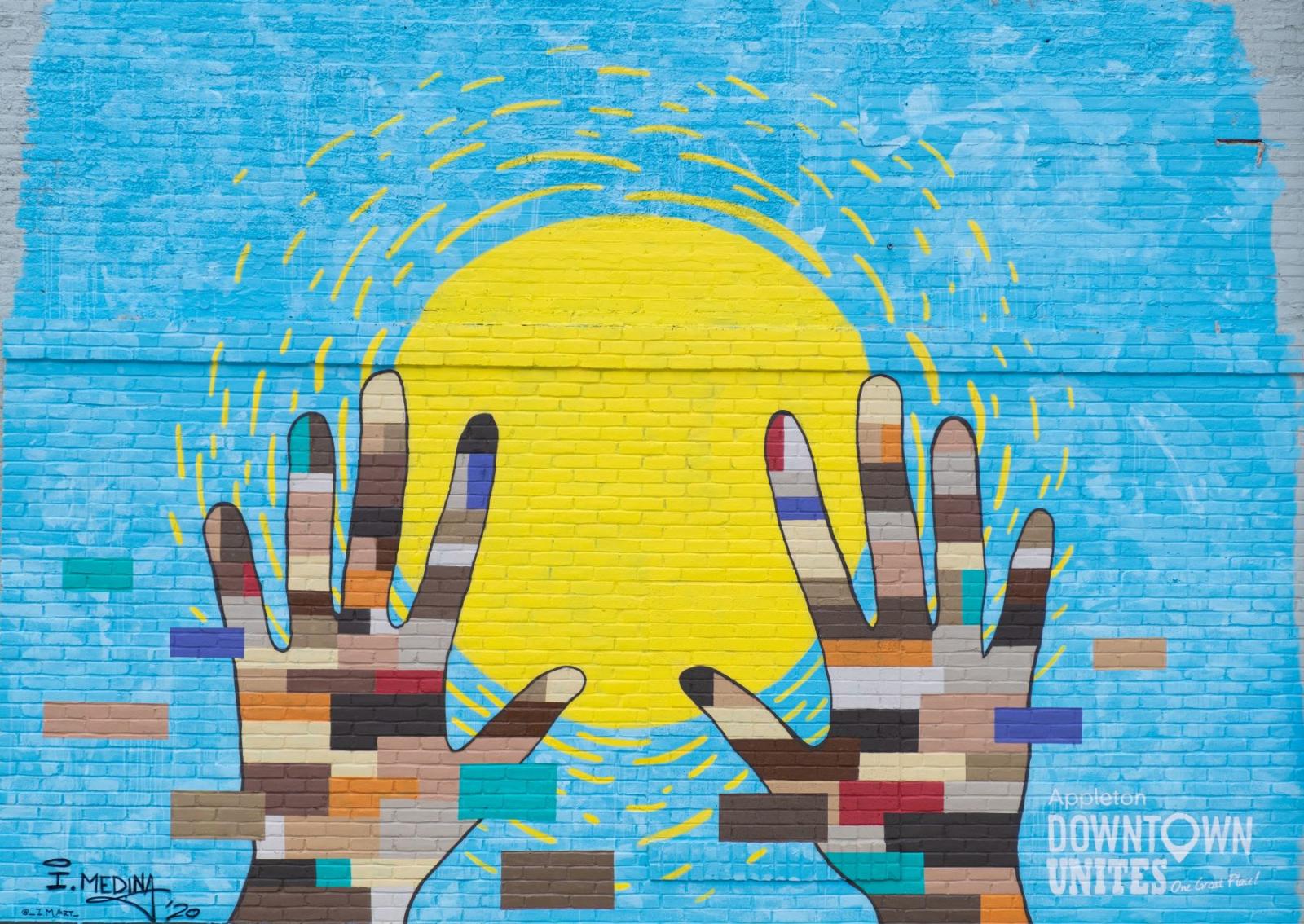 mural of the sun with hands covered in different shades of skin tones and flag colors