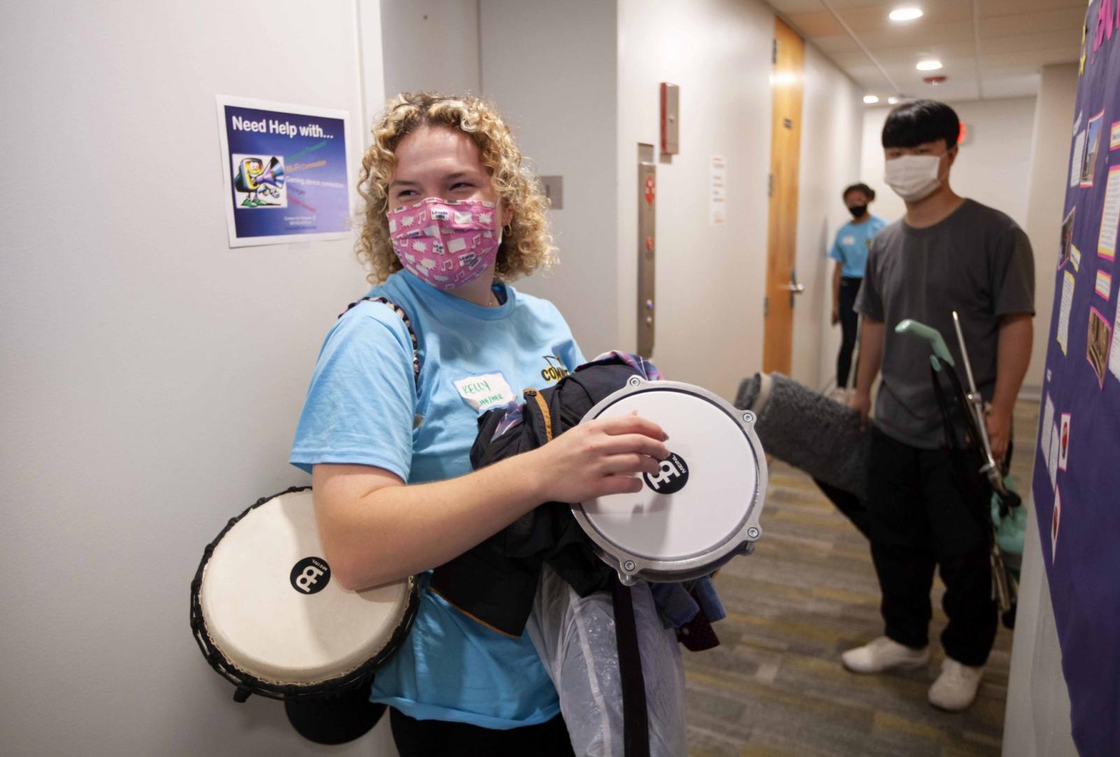 Student in mask carries instruments down a dorm hall during Move-In day.