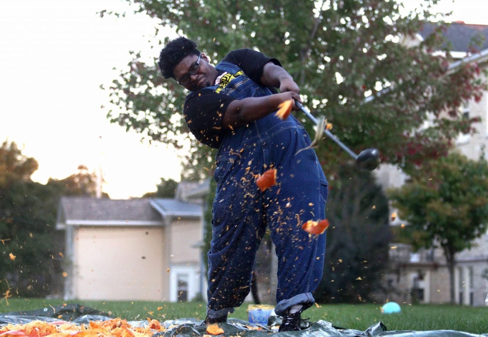 Student smashing a pumpkin with golf club during a Beta Theta Phi charity event.