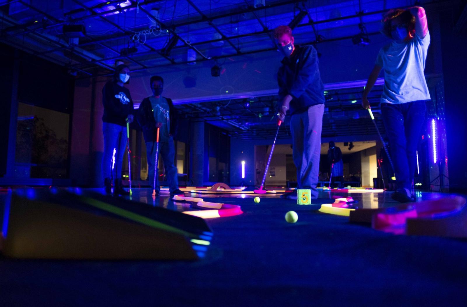 Four students playing glow-in-the-dark mini golf.