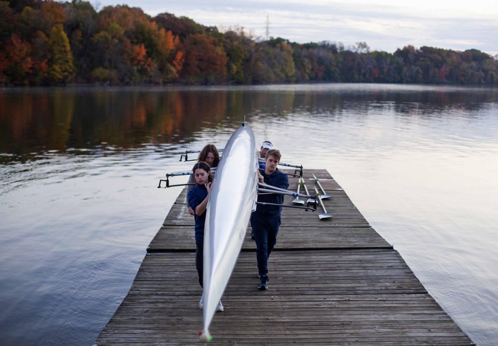 Four students carrying their boat back to shore after a morning of rowing.